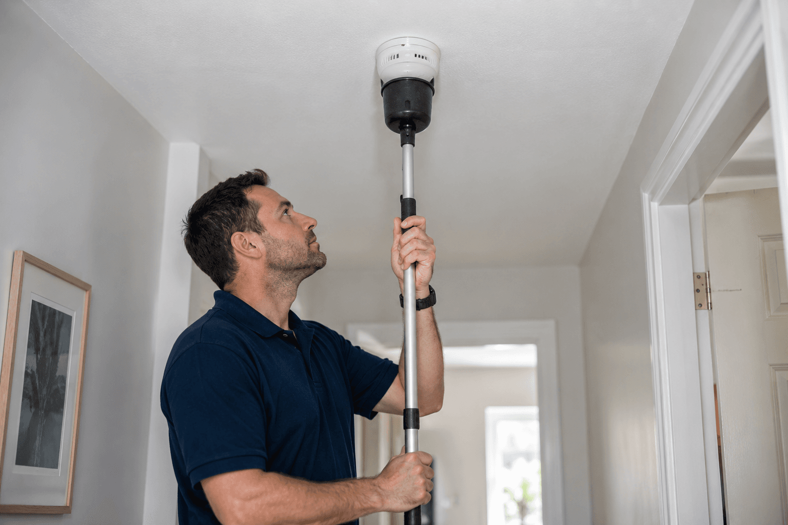Engineer testing a ceiling-mounted smoke alarm with a test pole in a London home